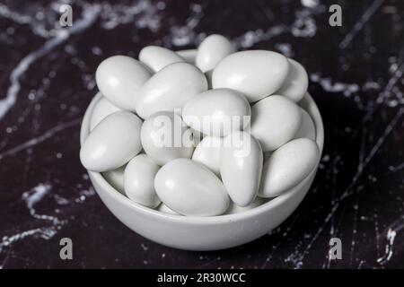 Chocolat et dragee aux amandes. Dragee au chocolat dans un bol en céramique sur fond sombre. Gros plan Banque D'Images