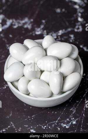 Chocolat et dragee aux amandes. Dragee au chocolat dans un bol en céramique sur fond sombre. Gros plan Banque D'Images