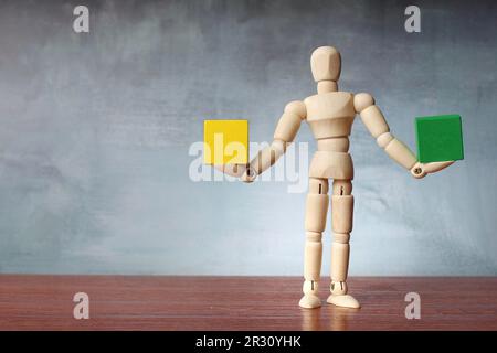 Figure humaine en bois équilibrant cube en bois vert et jaune avec espace de copie pour le texte. Harmonie, stabilité et concept de comparaison Banque D'Images