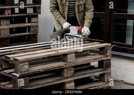 Procédé de ponçage du bois à l'aide d'une ponceuse à bande électrique portative. ponçage à la machine de la surface en bois sur établi. Banque D'Images