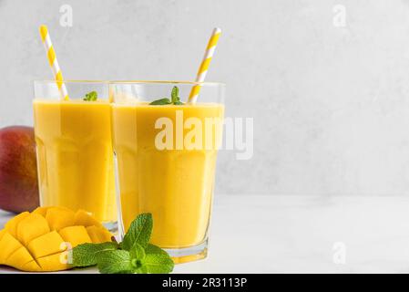 Smoothie à la mangue tropicale rafraîchissante dans un verre avec des fruits frais, de la menthe et de la paille sur fond de béton gris Banque D'Images