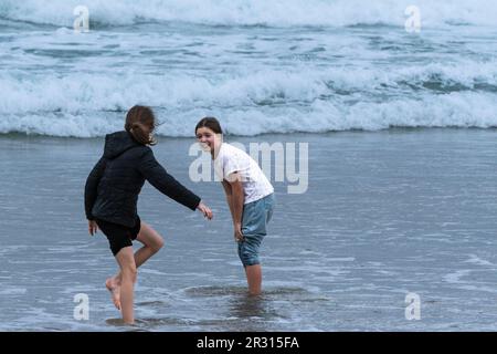 Deux jeunes adolescentes pagayent dans la mer par temps froid à Fistral à Newquay, en Cornouailles, en Angleterre, au Royaume-Uni. Banque D'Images