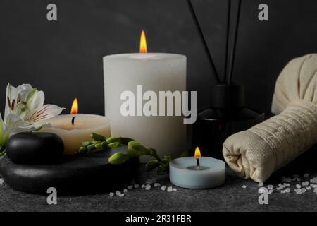 Belle composition de spa avec différents produits de soins et bougies allumées sur table gris foncé sur fond noir Banque D'Images