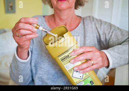 Femme qui se déchire d'une aiguille usagée dans une unité d'élimination des déchets Sharpsguard ou dans une poubelle pour objets pointus et tranchants Banque D'Images