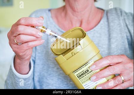 Femme qui se déchire d'une aiguille usagée dans une unité d'élimination des déchets Sharpsguard ou dans une poubelle pour objets pointus et tranchants Banque D'Images