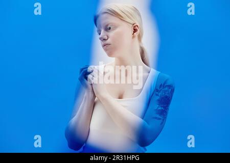 Portrait minimal de la jeune femme avec albinisme posant en bleu couleur, espace de copie Banque D'Images