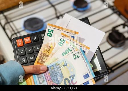 Paiement des factures de services publics, calculs sur une calculatrice. Les billets d'euro et de dollar sont près d'un brûleur à gaz en feu. Le concept d'augmenter le coût de nat Banque D'Images