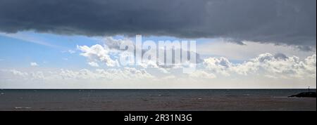 pluie tombant des nuages de tempête au-dessus d'une mer sombre avec le ciel bleu au loin Banque D'Images