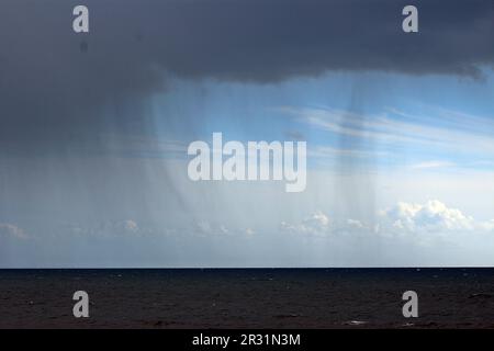 pluie tombant des nuages de tempête au-dessus d'une mer sombre avec le ciel bleu au loin Banque D'Images