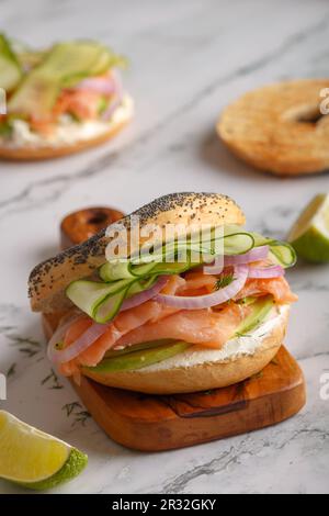 Sandwich au bagel de saumon avec fromage à la crème, avocat, oignons, concombre sur une planche de bois. Gros plan. Copier l'espace Banque D'Images