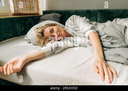 Belle femme en pyjama se trouve sur le lit le matin. Banque D'Images