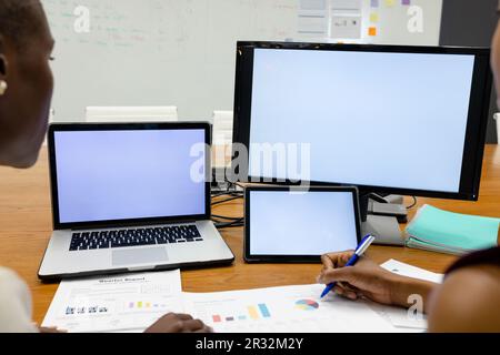 Image rognée de collègues afro-américains analysant des rapports par ordinateur portable et ordinateur de bureau Banque D'Images