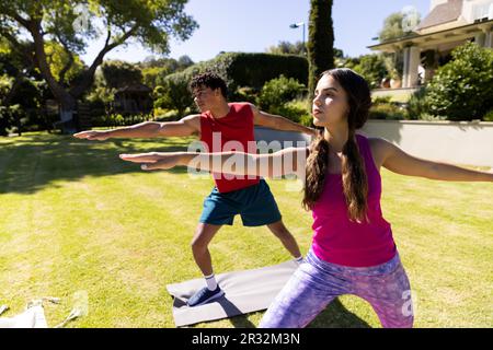 Joyeux couple de forme diverse pratiquant le yoga debout et s'étirant dans le jardin ensoleillé Banque D'Images
