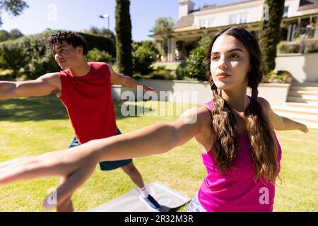Joyeux couple de forme diverse pratiquant le yoga debout et s'étirant dans le jardin ensoleillé Banque D'Images