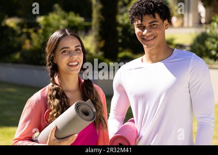 Portrait de Happy Fit divers couple debout dans le jardin ensoleillé tenant des tapis de yoga Banque D'Images