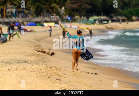 Une chatesurfer femelle marche le long de la plage en tenant sur le conseil et la barre de son cerf-volant à Mui ne, Vietnam. Banque D'Images