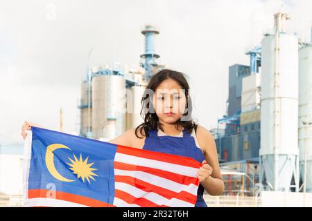 Triste jeune femme avec drapeau de la Malaisie contre fond d'usine Banque D'Images