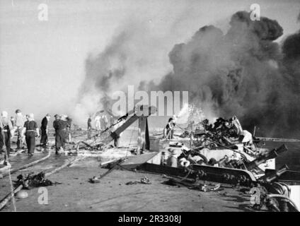 Les pompiers sont occupés à bord du HMS FORMIDABLE après qu'un avion-suicide japonais s'est écrasé sur le pont de vol alors qu'elle était en opération au large des îles Sakishima pour soutenir le débarquement d'Okinawa. Le pont de vol est parsemé d'épaves et de fumée noire coule des feux encore en feu à l'extrémité du pont de vol. Banque D'Images