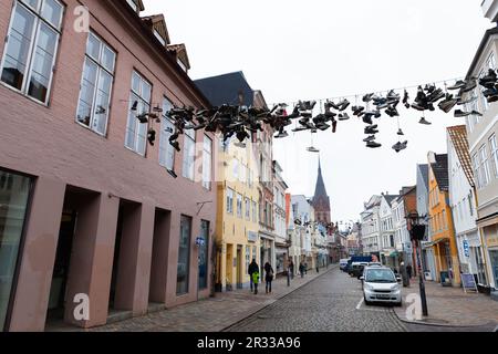 Flensburg, Allemagne - 10 février 2017: Beaucoup de chaussures sportives pendent sur les fils. Les gens ordinaires marchent dans la rue de la vieille ville de Flensburg Banque D'Images