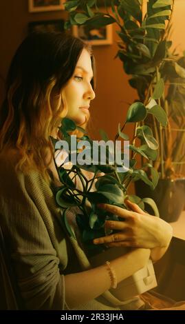 Portrait d'une belle jeune femme blonde vêtue à la maison, qui épouse une plante de maison qu'elle a grandi elle-même. L'amour des plantes et du jardinage à la maison. Débit Banque D'Images