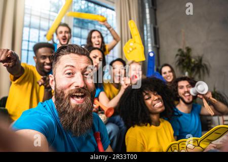 Un heureux supporter qui prend le selfie avec des fans de sport joyeux et multiethniques tout en regardant un match à la télévision à la maison - des amis célébrant la victoire quand l'équipe de sport gagne Banque D'Images