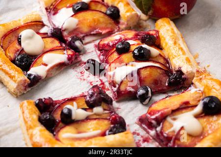 Tarte feuilletée à la nectarine et aux myrtilles avec glaçage à la vanille coupée en portions carrées sur un papier à pâtisserie Banque D'Images