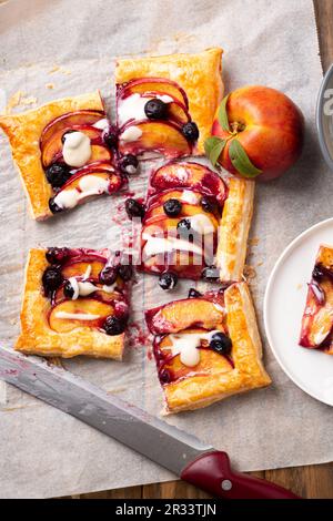 Tarte feuilletée à la nectarine et aux myrtilles avec glaçage à la vanille coupée en portions carrées sur un papier à pâtisserie Banque D'Images