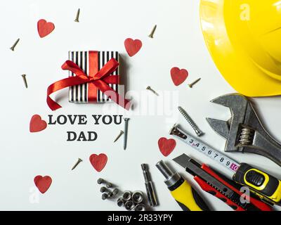 Outils de construction, casque et boîte cadeau enveloppée avec un noeud sur fond blanc avec Love You papa. Carte de vœux de construction pour papa le jour des Pères. Banque D'Images