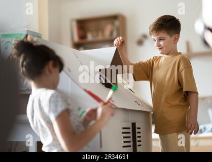 Des enfants heureux peignant une maison en carton faite à la main ensemble. Banque D'Images