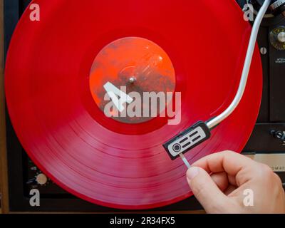 Détail d'une main masculine plaçant l'aiguille sur la piste d'un disque en vinyle rouge. Plateau tournant vintage Banque D'Images