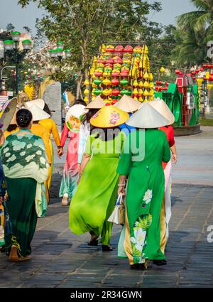 Vue arrière d'un groupe de femmes portant des robes traditionnelles vietnamiennes marchant dans la vieille ville de Hoi an par une journée ensoleillée. Banque D'Images