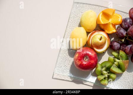 Plateau de fruits - les fruits, mangues, Oranges, fraises, bleuets kiwi Pamplemousse Raisins, bananes pommes sur la plaque blanche, sur l'off white tabl Banque D'Images