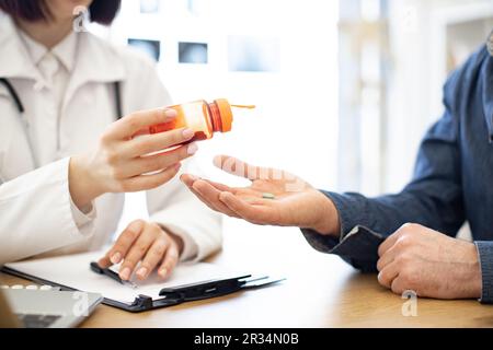 Gros plan de brunette médecin versant des comprimés de la bouteille d'orange sur la main du patient dans la polyclinique moderne. Homme prenant des pilules pour réduire les symptômes de la maladie et de la douleur. Concept de santé et de traitement. Banque D'Images