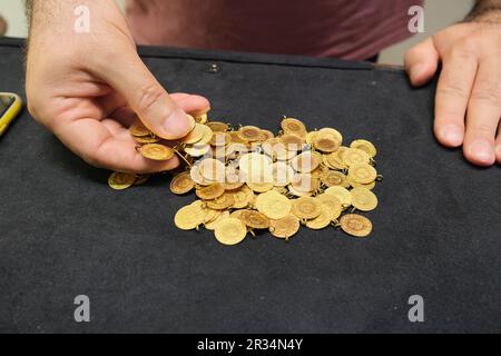 Main d'homme tenant une pièce de monnaie en or de quart turc sur un fond noir. Banque D'Images