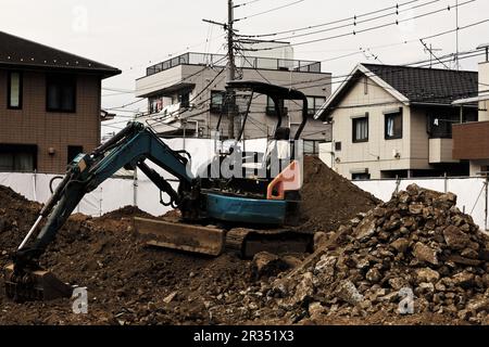 Un chantier de génie civil dans une zone résidentielle où une petite pelle hydraulique est utilisée pour niveler le sol Banque D'Images