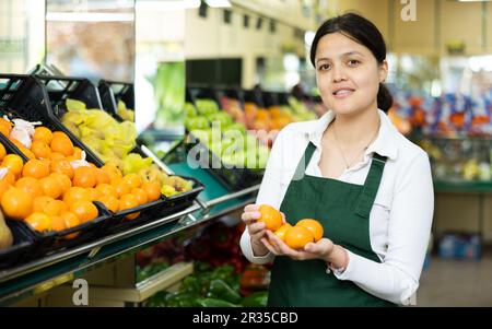 Une jeune femme en uniforme vend des mandarines à l'épicerie Banque D'Images