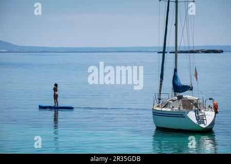 Jeune femme pratiquant le paddle surf à côté d'un voilier, Cala Portals Vells, Calvia, Majorque, Iles Baléares, Espagne. Banque D'Images