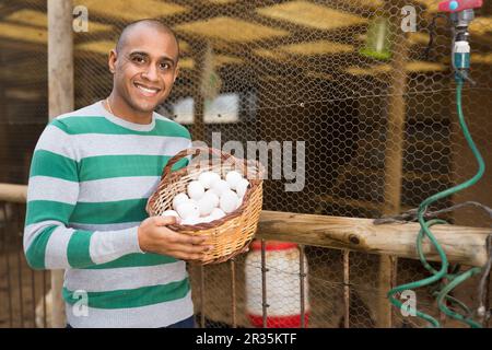 Homme souriant tient un panier d'œufs de poulet dans ses mains. Banque D'Images