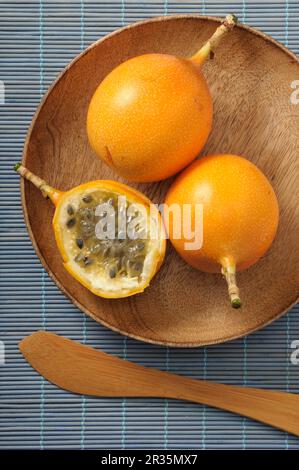 Fruits de la passion jaunes, entiers et coupés en deux, sur une assiette en bois Banque D'Images