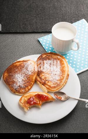 Crêpes au babeurre avec sucre glace et confiture de fraise sur une assiette avec une tasse de lait Banque D'Images