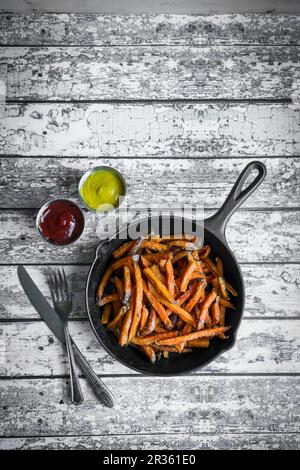 Frites de patate douce dans une poêle en fonte sur une surface rustique en bois Banque D'Images