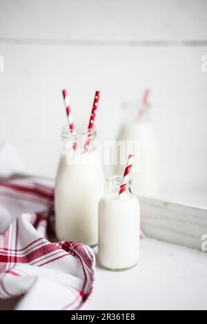 Bouteilles de lait avec du rouge et blanc pailles à rayures sur une surface en bois blanc Banque D'Images