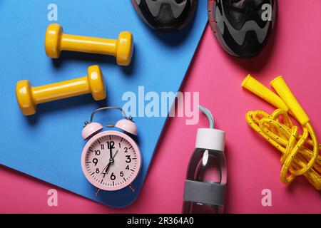 Réveil, bouteille d'eau et équipement sportif sur fond rose, posé à plat. Exercice du matin Banque D'Images