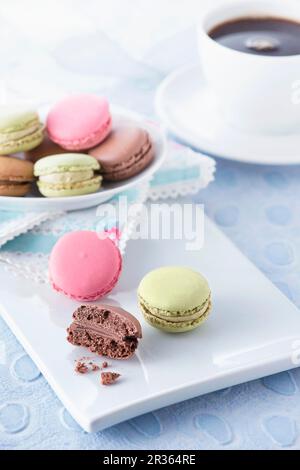 Macarons sur un plateau blanc sur une surface bleu clair avec une tasse de café en arrière-plan Banque D'Images