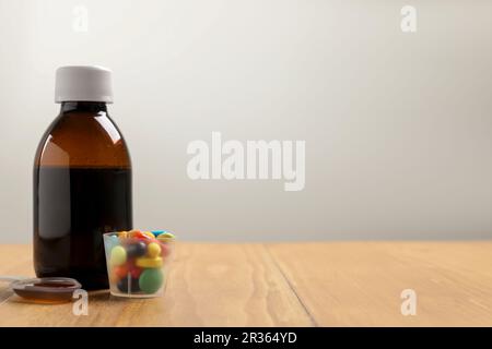 Bouteille de sirop, cuillère à doser et tasse à mesurer avec des pilules sur une table en bois sur fond blanc, espace pour le texte. Médecine du froid Banque D'Images