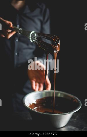 Le chocolat liquide s'égoutte d'un fouet dans un bol en acier inoxydable Banque D'Images