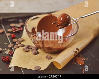 Truffes de massepain faites maison enrobées de chocolat noir, qui s'égoutte dans un bol en verre sur un morceau de papier de cuisson Banque D'Images