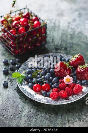 Baies fraîches sur une assiette et cerises aigres dans un panier en fil de fer Banque D'Images