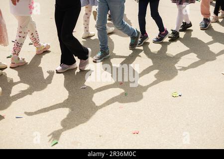 Groupe d'enfants méconnaissables en vêtements d'été décontractés marchant dans une colonne sur la route asphaltée. Coupe courte, jambes pour enfant. Concept de style de vie de loisirs. Été Banque D'Images