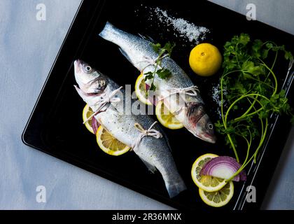 Deux poissons branzino farci aux herbes, l'oignon et les tranches de citron sur une plaque de cuisson Banque D'Images